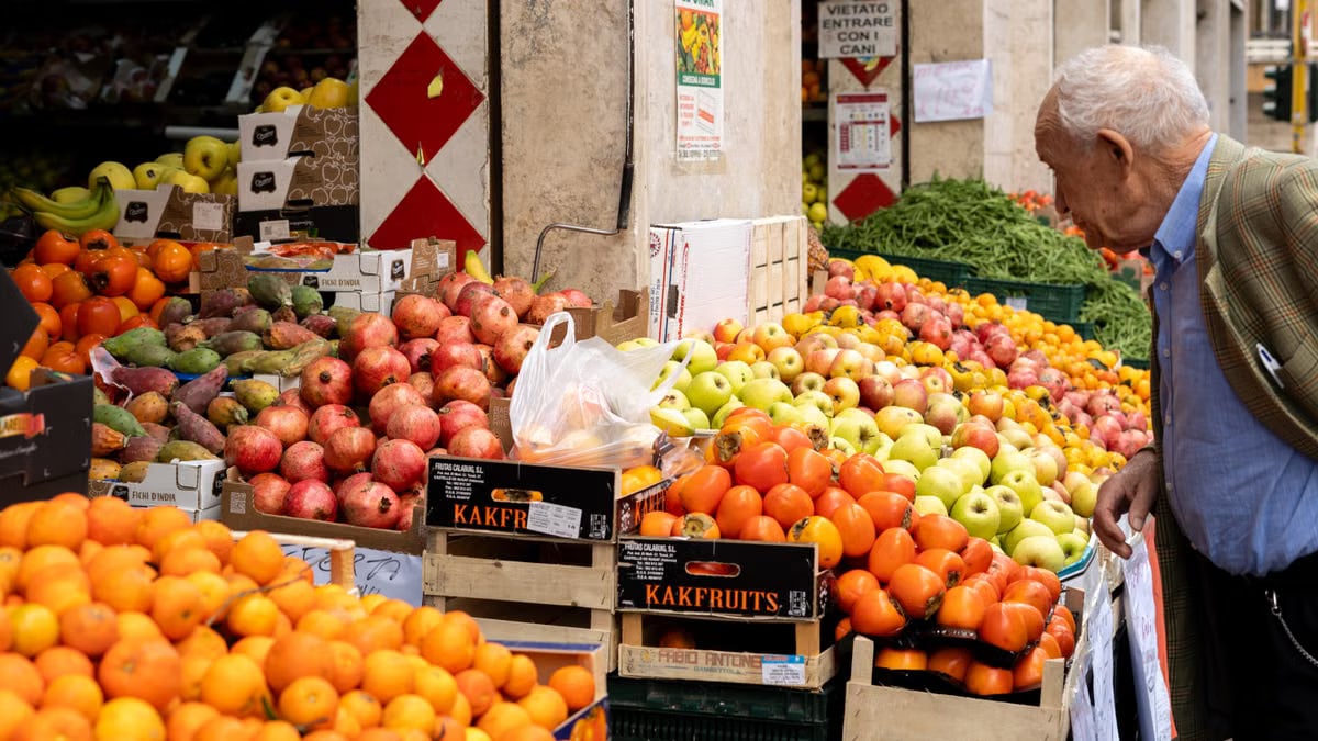 Senior man browsing vibrant fruit selection at an outdoor market in Rome, Lazio, Italy.
